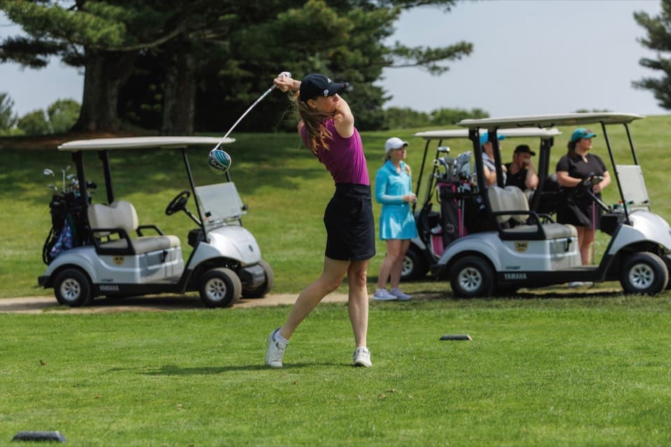 Golfer teeing off with carts in background